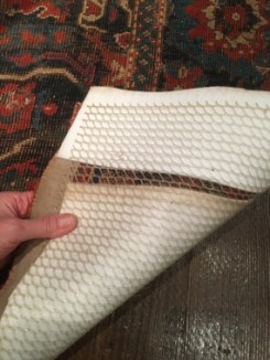 Hand holding back edge of carpet to show backside
